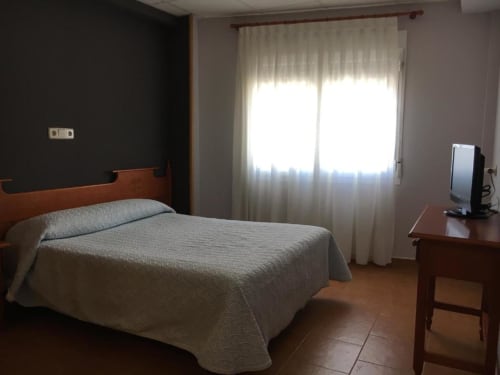 Amplia habitación doble en Hostal Imaginatelo con cama de madera, colcha crema, escritorio, TV y ventana luminosa con vistas a la ciudad