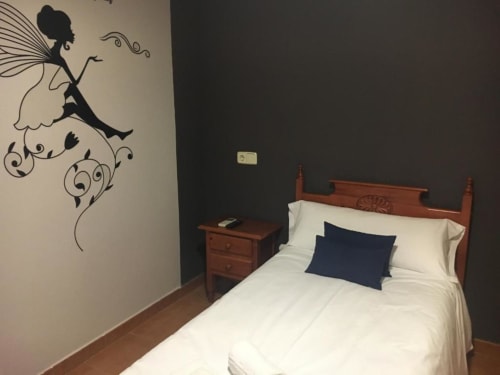 Habitación individual en Hostal Imaginatelo con mural de hadas, cama de madera, sábanas blancas y pared de acento oscuro.