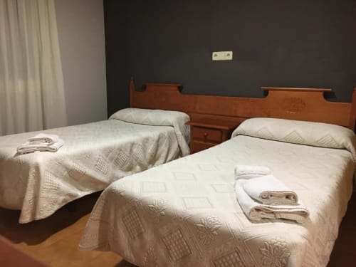Camas gemelas con colchas acolchadas crema y toallas en el Hostal Imaginatelo de Carrascosa del Campo