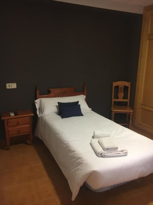 Habitación individual en Hostal Imaginatelo de Carrascosa del Campo con cama de madera, sábanas blancas, paredes oscuras y muebles de madera