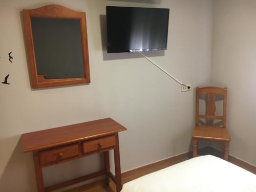 Habitación individual en Hostal Imaginatelo con muebles de madera, TV de pared, espejo y escritorio en Carrascosa del Campo
