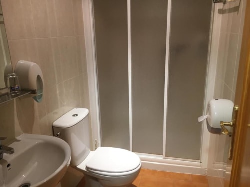 Baño moderno del Hostal Imaginatelo con inodoro blanco, lavabo y ducha con azulejos, paredes en tonos beige