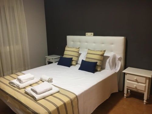 Habitación deluxe en Hostal Imaginatelo con ropa de cama a rayas amarillas, cabecero crema, almohadas azul marino y mesitas de noche