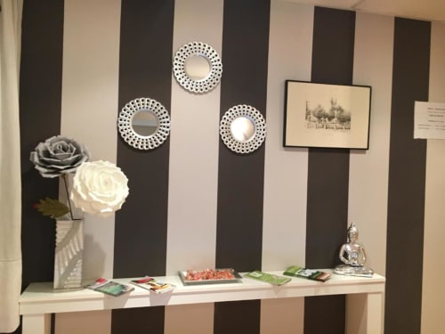 Estante decorativo en Hostal Imaginatelo con pared rayada, espejos ornamentales, rosas blancas y cuadros enmarcados
