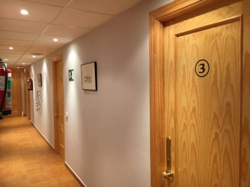Pasillo del Hostal Imaginatelo con puerta de madera numerada 3, paredes blancas e iluminación empotrada