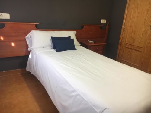 Habitación individual en Hostal Imaginatelo con cama de madera, ropa de cama blanca, almohada azul marino y paredes oscuras en Carrascosa del Campo