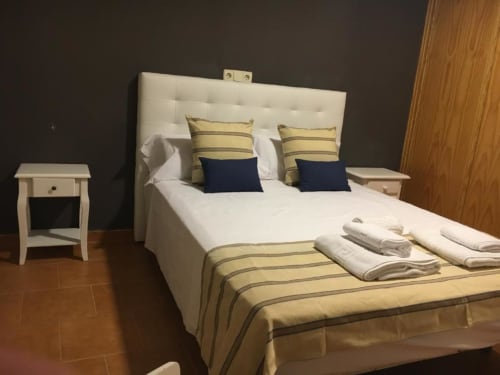 Habitación deluxe en Hostal Imaginatelo con cama queen, cabecero blanco, ropa de cama con rayas doradas, almohadas azul marino y detalles de madera