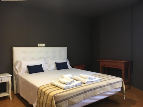 Habitación deluxe en Hostal Imaginatelo, Carrascosa del Campo, con cama tapizada blanca, almohadas azul marino y muebles de madera
