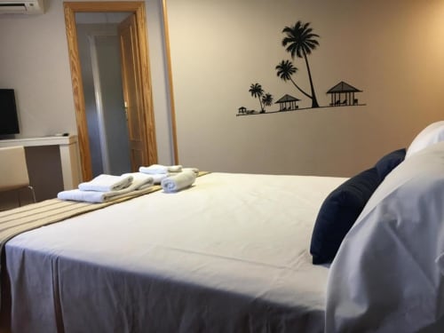 Habitación deluxe en Hostal Imaginatelo con ropa de cama blanca, decoración tropical y vistas a la ciudad en Carrascosa del Campo
