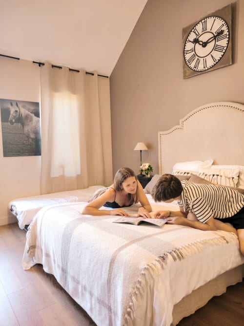 Mère et enfant lisant ensemble dans la Chambre Orion du Paddock B&B, La Drenne, avec vue sur le jardin