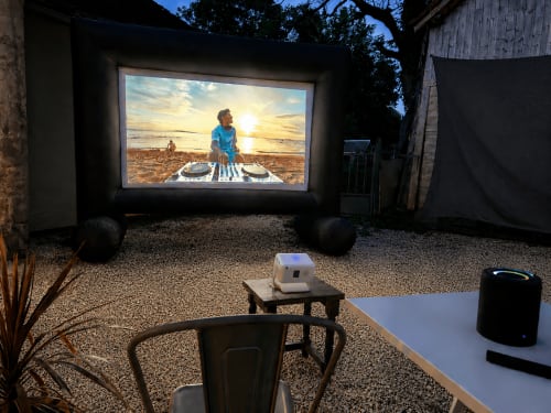 Cinéma privé en plein air à Domaine Valenquercy avec grand écran affichant une scène de plage, projecteur et haut-parleurs noirs