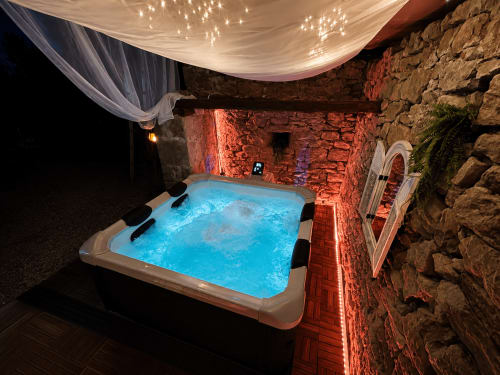 Bain à remous illuminé aux eaux bleues dans la cour en pierre du Domaine Valenquercy, auvent drapé, murs de briques rustiques