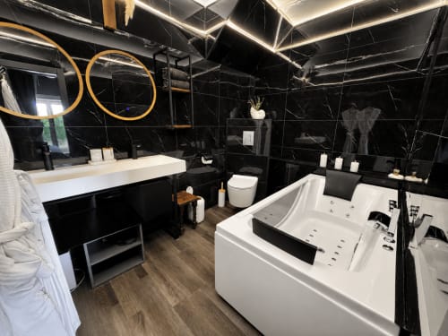 Salle de bain spa luxueuse aux murs en marbre noir, miroirs dorés, lavabo blanc et baignoire jacuzzi au Domaine Valenquercy