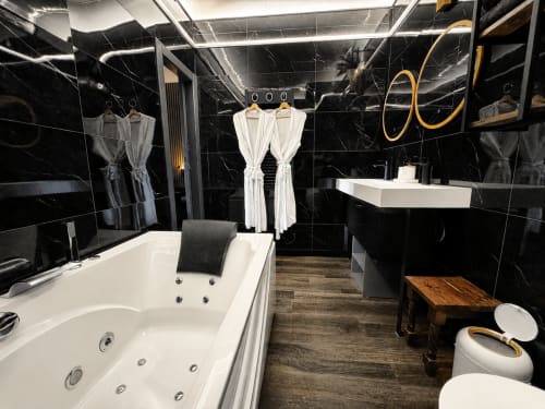 Salle de bain luxueuse avec baignoire Jacuzzi, murs en marbre blanc et finitions dorées à la suite Domaine Valenquercy du Vignon-en-Quercy