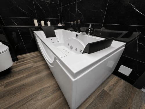 Baignoire balnéo luxueuse aux murs en marbre noir et parquet dans la Suite & Spa du Domaine Valenquercy