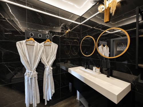 Salle de bain en marbre noir moderne au Domaine Valenquercy avec lavabo blanc, miroirs dorés et peignoirs dans ce luxueux gîte français