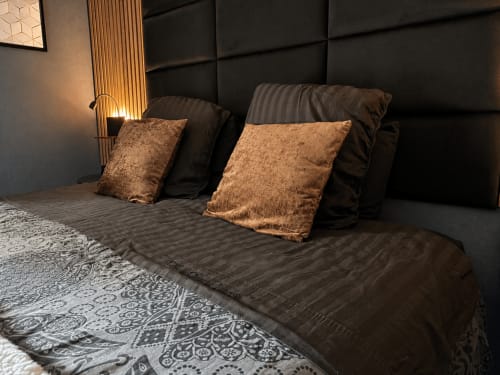 Chambre de luxe au Domaine Valenquercy avec tête de lit capitonnée noire, coussins bronze et literie à motifs, vue sur jardin