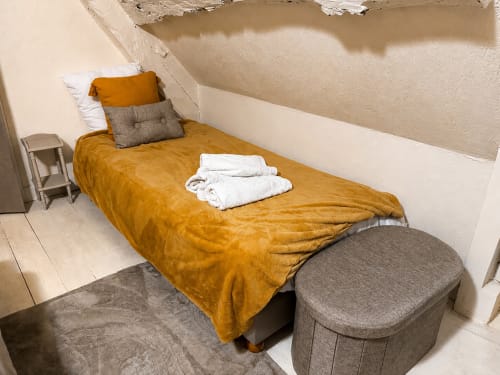 Cozy bedroom at Domaine Valenquercy with golden bedspread, white pillows, gray cushioned bench, and Jacuzzi amenities in Le