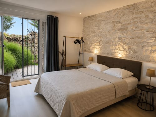 Chambre moderne à La Bastide Des Muriers avec vue sur jardin, mur en pierre et portes-fenêtres ouvertes sur un paysage verdoyant
