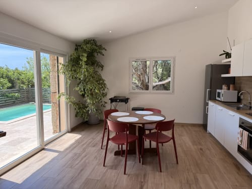 Salle à manger cottage moderne avec vue sur piscine, table ronde, chaises rouges, cuisine ouverte et accès à piscine privée chauffée