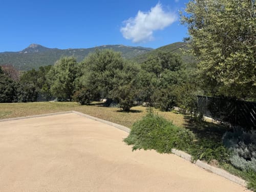 Sandy driveway and private backyard of A Santa villa in Figari, Corsica, with olive trees and mountain views