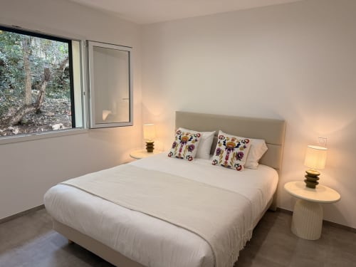 Modern bedroom in A Santa villa, Figari with white bed, colorful pillows, bedside lamps, and mountain view window