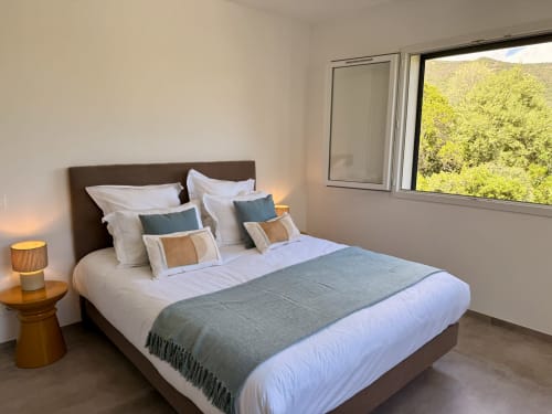 Modern bedroom with brown headboard, white bedding, grey throw, and mountain views at In Casa Conciergerie villa in Figari
