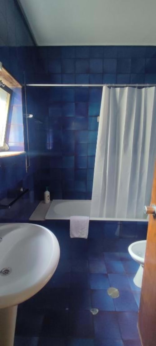 Modern bathroom at Porta 80 House hotel in Braga with navy blue tiles, white sink, and bathtub with shower curtain