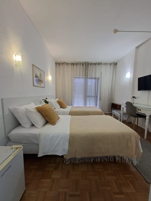 Twin bedroom at Porta 80 House hotel in Braga with city view balcony, modern furnishings, TV, and work desk