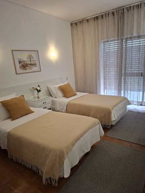 Quarto duplo da Porta 80 House em Braga com duas camas, mobiliário moderno e acesso a varanda com vista para a cidade através de cortinas