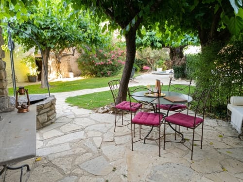 Patio ombragé avec chaises en fer forgé et coussins bordeaux à l'hôtel La Bastide Des Muriers à Deaux, France
