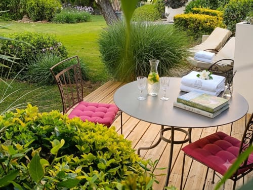 Terrasse de jardin élégante à La Bastide Des Muriers avec table ronde, chaises rembourrées bordeaux et jardins soignés à Deaux