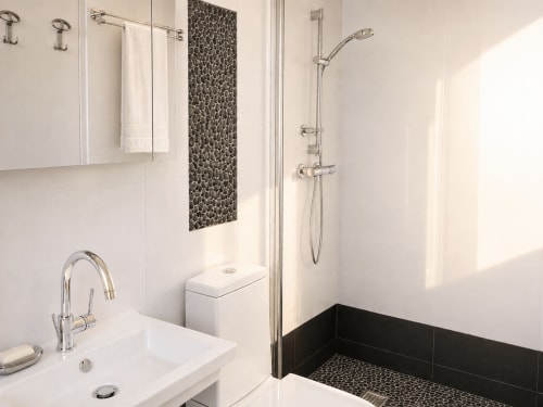 Salle de bain moderne aux murs blancs, mur d'accent en galets noirs, douche pluie et robinetterie chromée au FETTOLINA