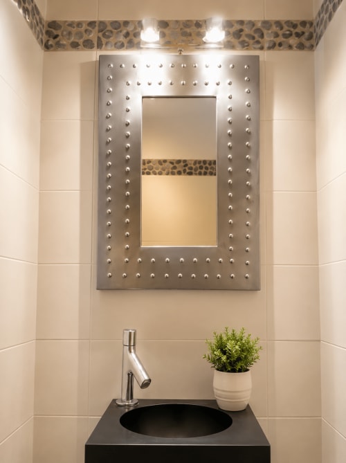 Lavabo de salle de bain moderne avec vasque noire, robinetterie chromée, plante en pot et miroir à cadre métallique clouté dans un appartement à Cannes