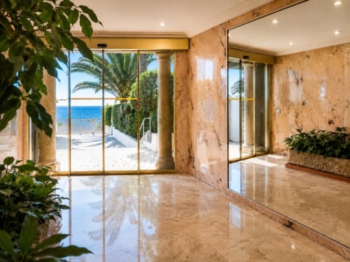 Appartement de luxe en bord de mer à Cannes avec sols en marbre, vue sur la mer et palmiers visibles par les portes vitrées