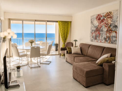 Appartement de luxe vue mer à Cannes avec canapé marron, salle à manger et vues panoramiques sur la Méditerranée depuis le balcon.