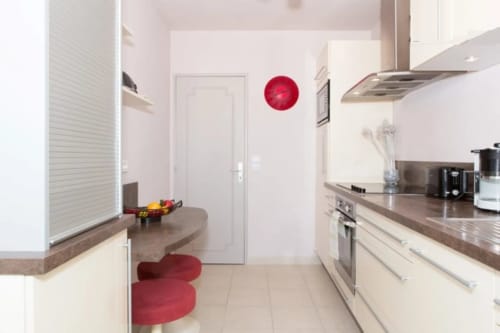 Cuisine contemporaine de l'appartement Le FETTOLINA à Cannes avec meubles blancs, plan de travail marron et touches rouges