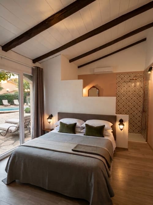 Chambre moderne à La Bastide Des Muriers avec lit queen-size, poutres apparentes, terrasse vue piscine et décoration style marocain