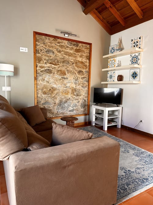 Cozy living room in Hidden Jewel Villa at Quinta Boa Vida with brown sofa, TV, stone wall, and decorative shelves.