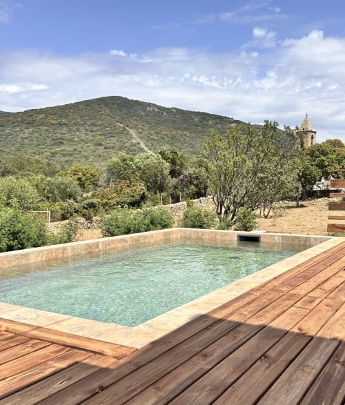 Private heated pool at In Casa Conciergerie cottage in Figari, with mountain views and bell tower visible in distance