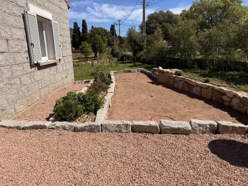 Cottage garden in Figari with gravel patio, stone borders, and private outdoor space surrounded by trees
