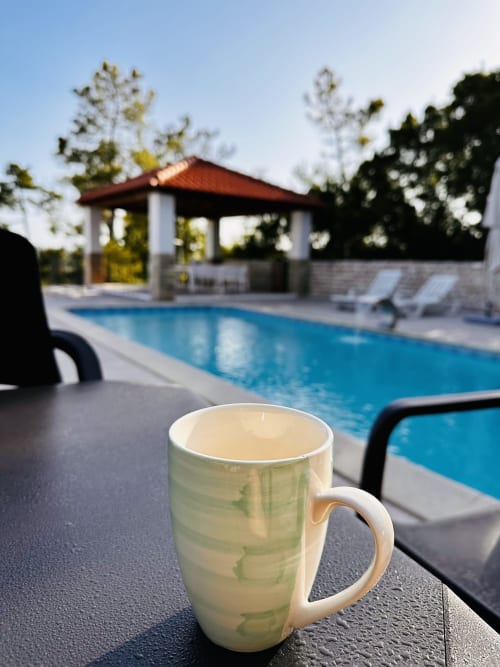 White mug with tea on poolside table at Quinta Boa Vida, Alcobaça, overlooking blue swimming pool and red-roofed pavilion