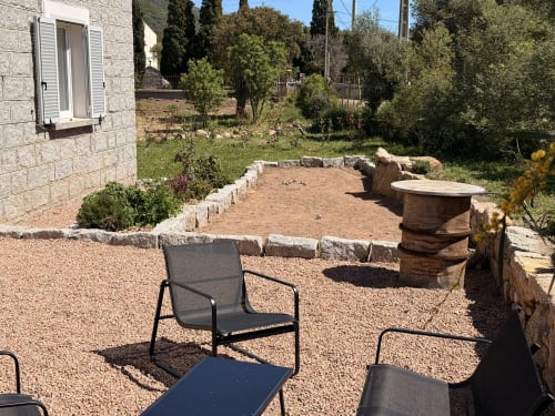 Patio rustique à In Casa Conciergerie à Figari avec zone de détente en gravier, foyer en pierre et vue sur le jardin