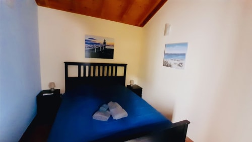 Cozy bedroom with blue bedding, black wooden bed frame, and mountain view artwork at Quinta Boa Vida chalet in Alcobaça