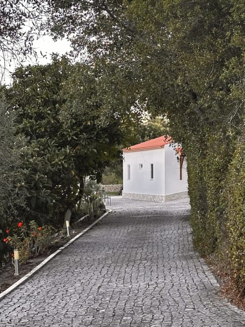 White cottage with terracotta roof at Quinta Boa Vida, surrounded by lush greenery and hedges, Alcobaça