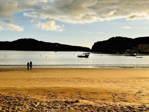Sandy beach cove with moored boats, forested cliffs, and cloudy sky near Alcobaça