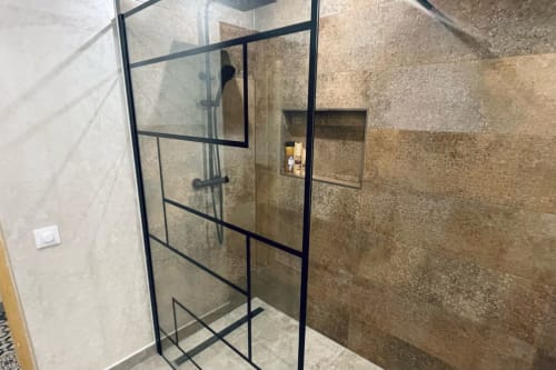 Cabine de duche moderna com porta de vidro com moldura preta e paredes de azulejos bronze no banheiro da casa El Sueño de Andalucia