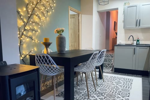 Área de refeições moderna em cottage andaluz com mesa preta, cadeiras brancas, decoração de galho iluminado e cozinha equipada