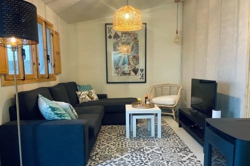Sala de estar moderna da casa de férias El Sueño de Andalucia na Espanha com sofá preto, cadeira de rattan e tapete com padrões geométricos