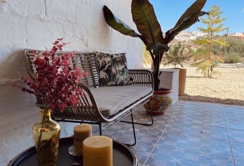 Terraço rústico da casa rural El Sueño de Andalucia com assentos de vime, flores vermelhas e vista para as montanhas em Huércal-Overa, Espanha